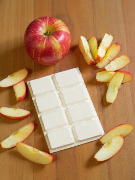 Apple Pickin’ wax melt on wood floor, with apple and apple slice surrounding it